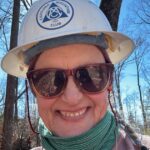 Appalachian Trail volunteer Bev McDowell smiles, wearing a Carolina Mountain Club hard hat and sunglasses.